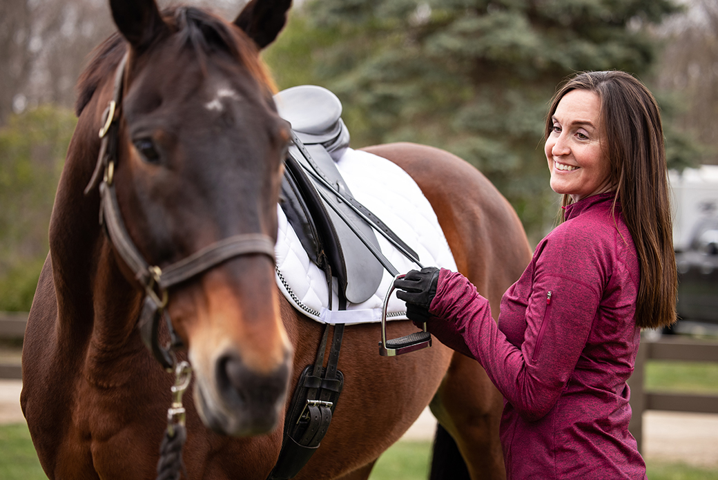 A woman holding on a stirrup on a brown horse